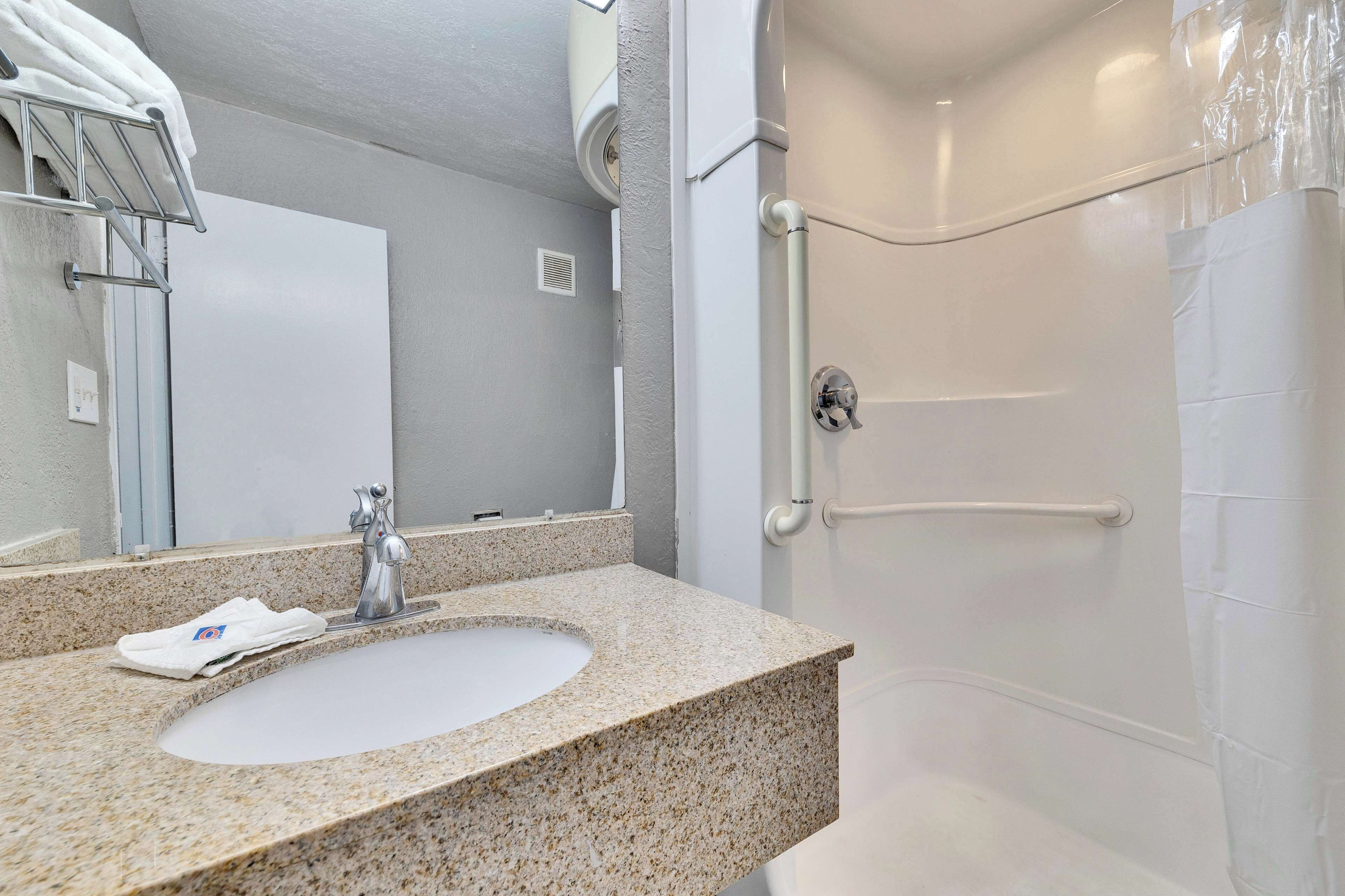 A bathroom with a granite countertop sink, a mirror, and a shower with a white door.
