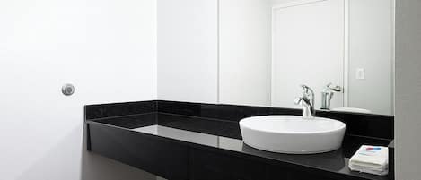 Un baño moderno con encimera negra, lavabo blanco y un espejo grande.