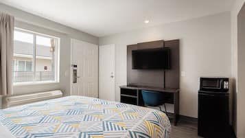 A hotel room with a bed, a desk with a chair, a TV, and a microwave.