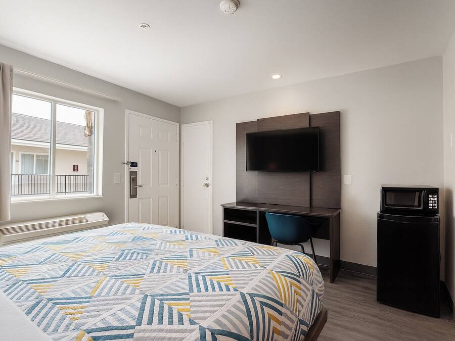 A hotel room with a bed, a desk with a chair, a TV, and a microwave.