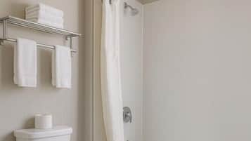 Un baño moderno con inodoro, ducha con cortina y repisa con toallas.