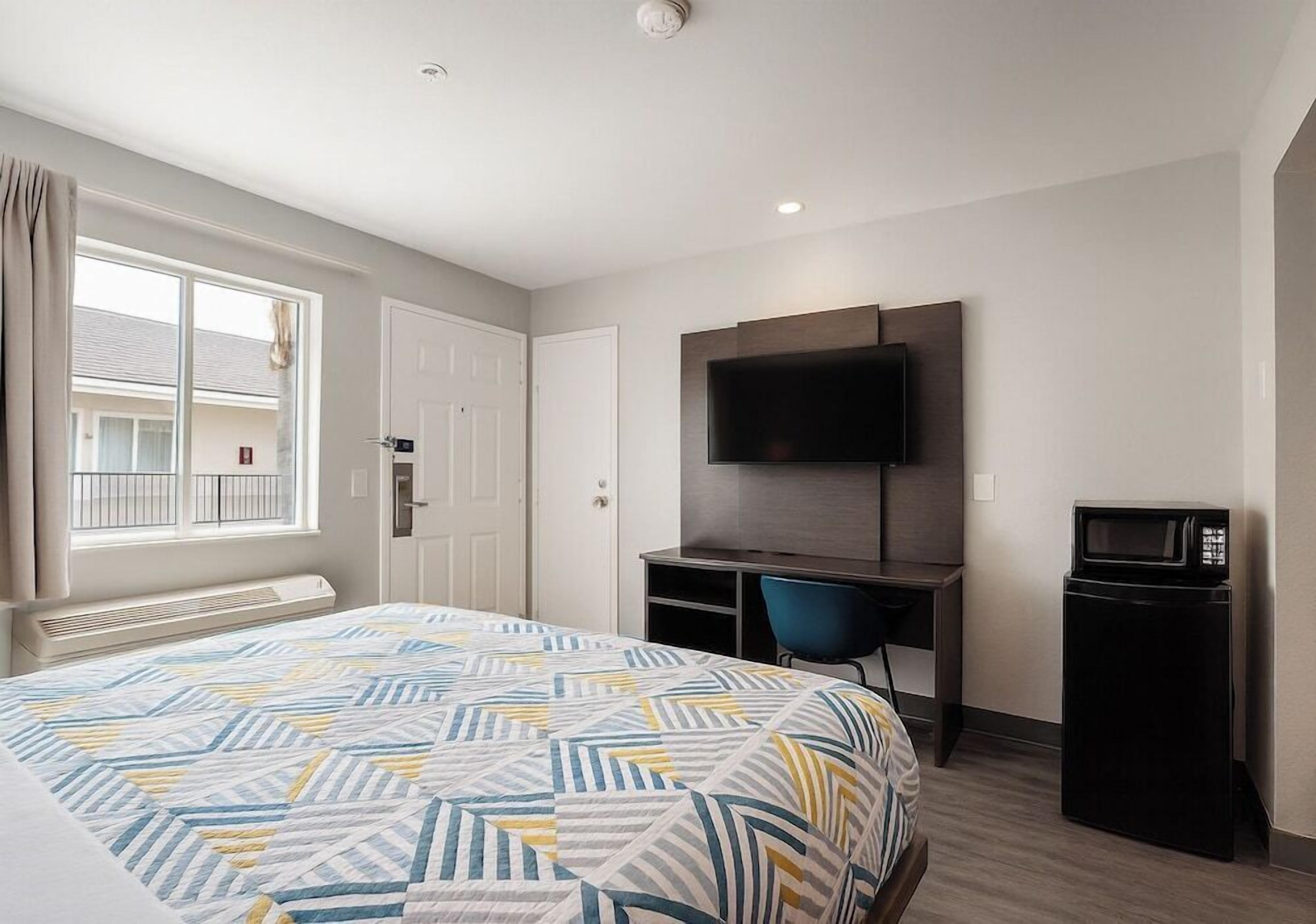 Una habitación de hotel con cama, escritorio, silla, televisor y microondas.