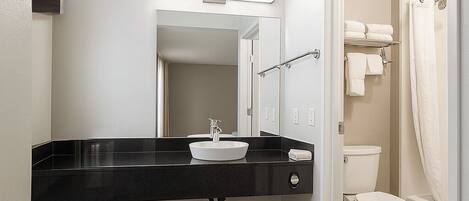 A modern bathroom with a black countertop sink, a mirror, a toilet, and a shower area.