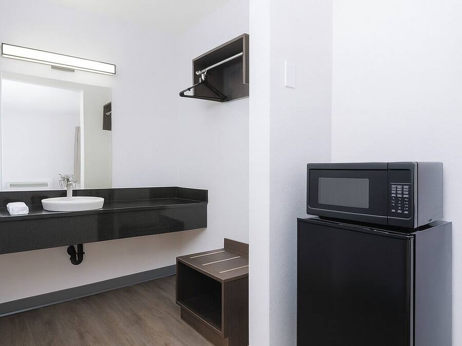 A modern bathroom with a black countertop, a sink, a mirror, and a black refrigerator.