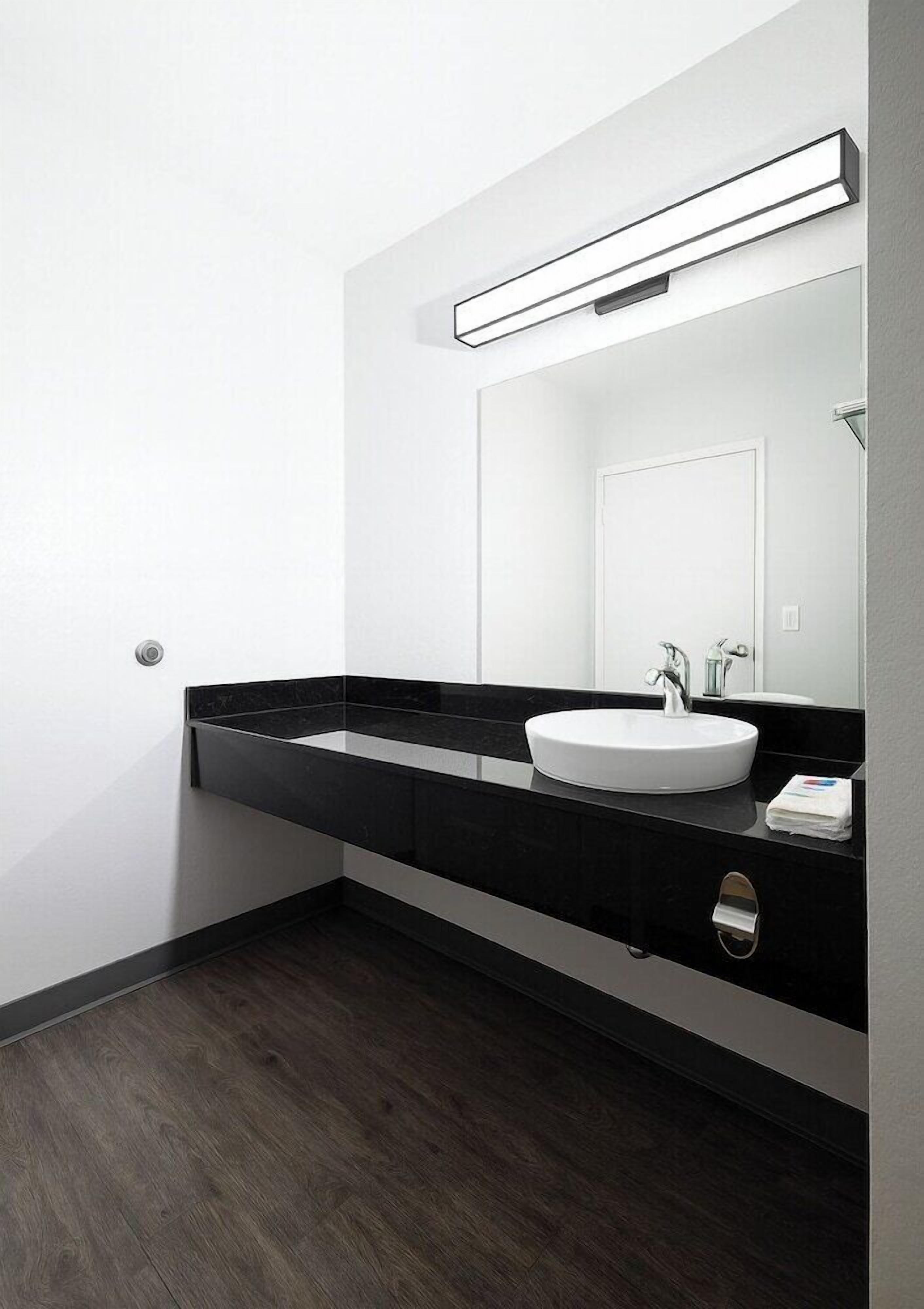 Un baño moderno con encimera negra, lavabo blanco y espejo encima.