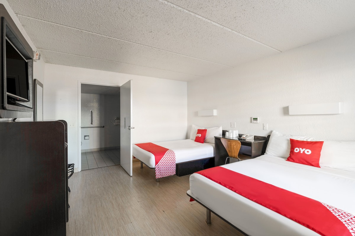 A hotel room with two beds, a desk, a TV, and a door leading to a bathroom.