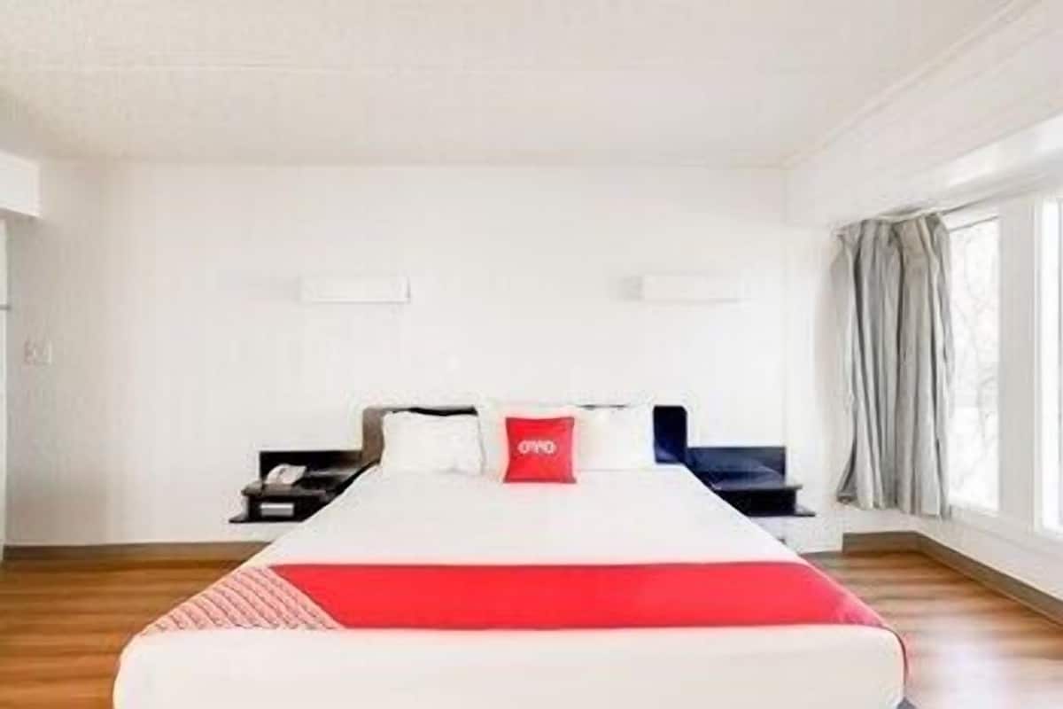 A hotel room with a large bed, a nightstand, a desk, and a window with curtains.