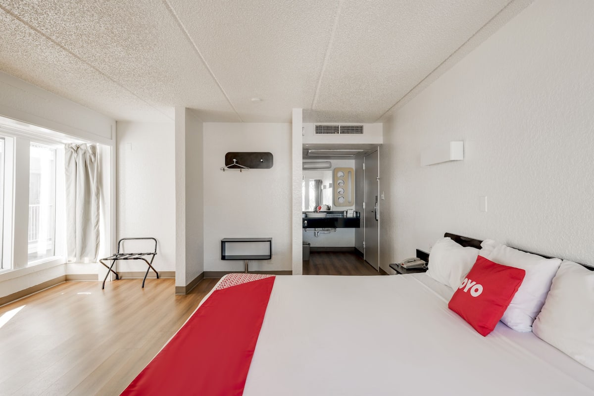 A hotel room with a bed, a desk, a chair, a TV, and a kitchenette.