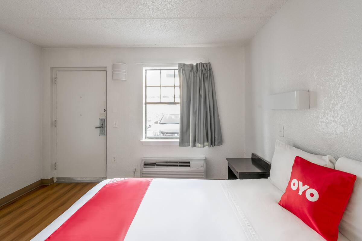 A hotel room with a bed, a window with curtains, a heater, and a door.