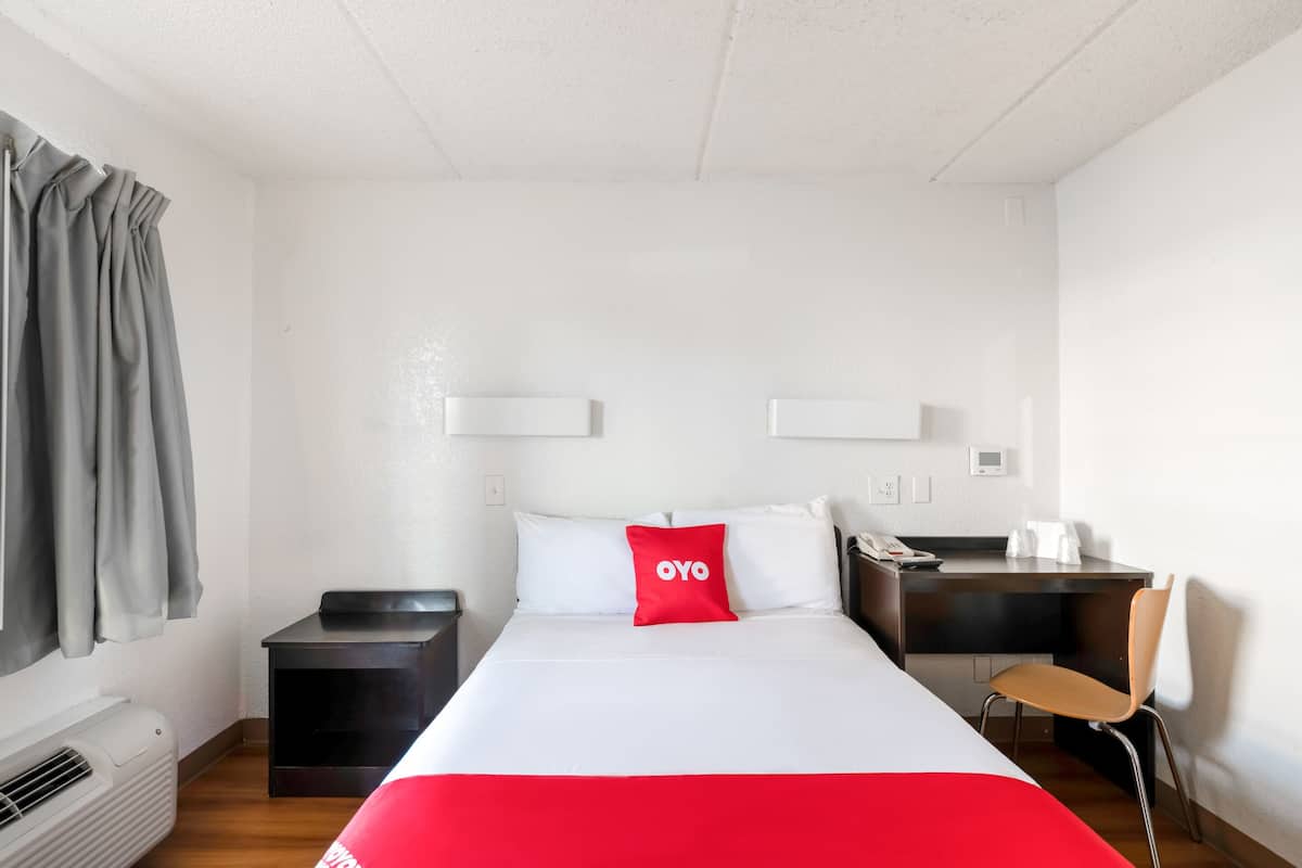 A hotel room with a bed, a desk, a chair, and a window with curtains.