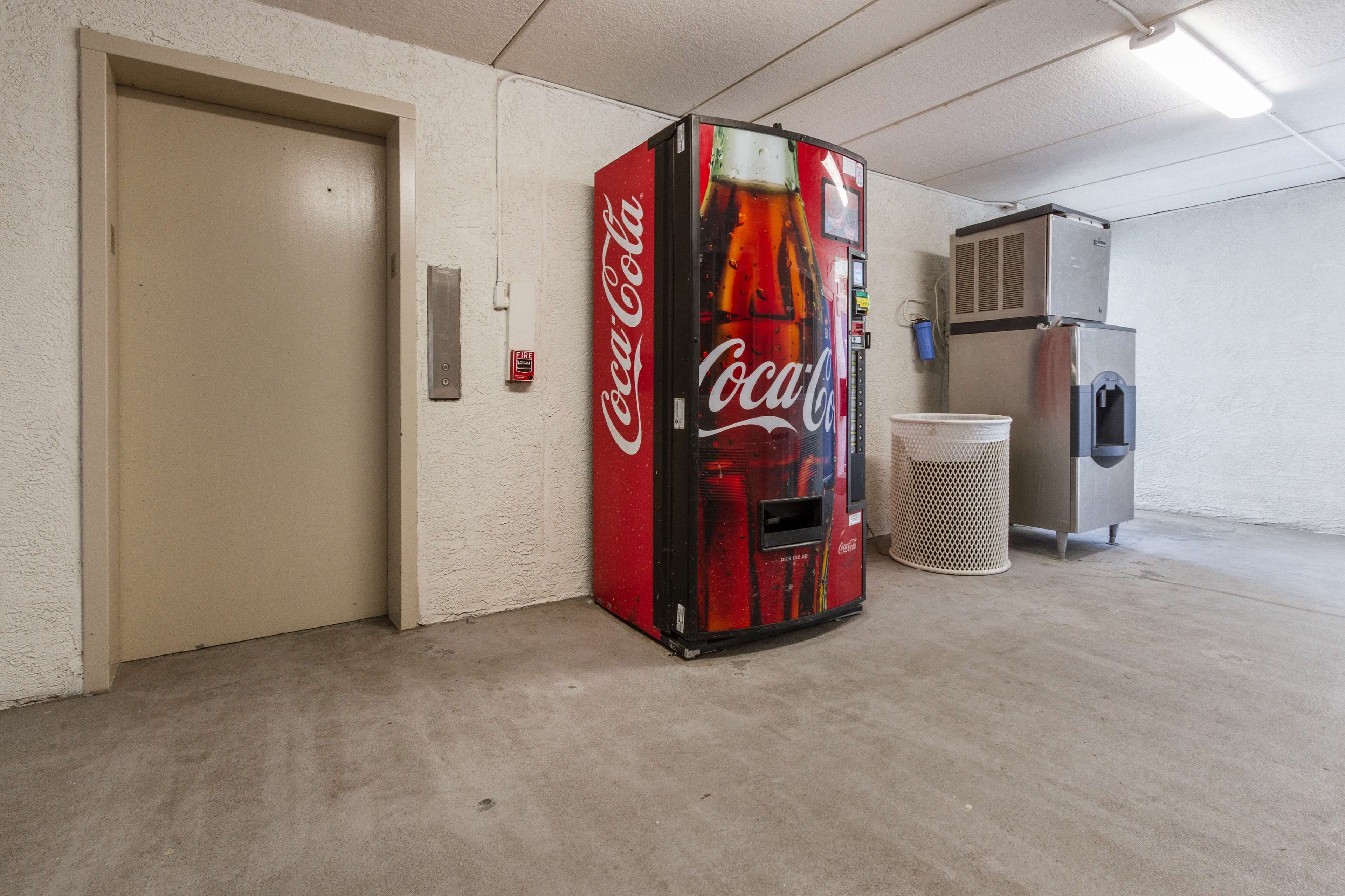 Un distributeur automatique de Coca-Cola situé dans un couloir, avec une porte et une poubelle à proximité.