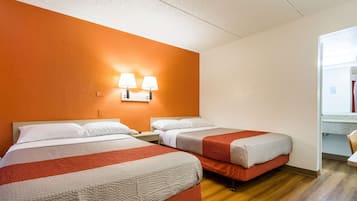 A hotel room with two beds, a wooden floor, and a bright orange accent wall.