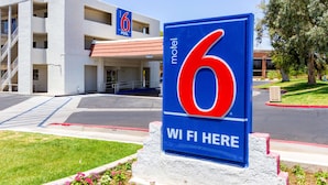 A motel sign with the number 6 and the text "WI FI HERE" in front of a building with a red roof and multiple floors. - Motel 6 Tempe, AZ – Phoenix Airport – Priest Dr (Tempe)