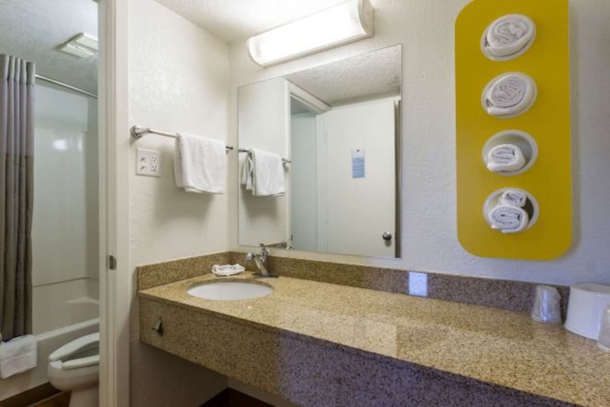 A bathroom with a granite countertop sink, a mirror, and a towel rack with folded towels.