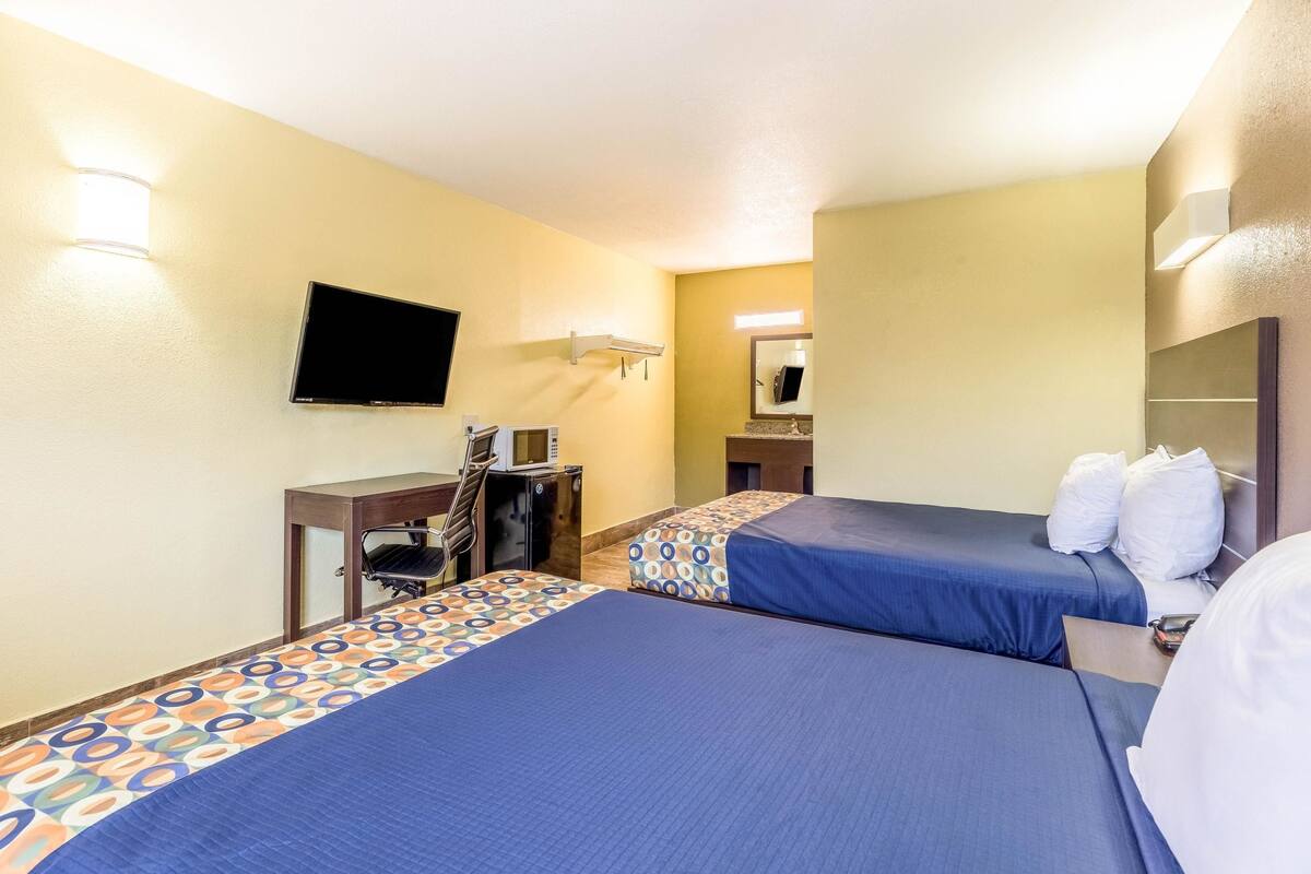 A hotel room with two beds, a desk, a television, and a mirror.