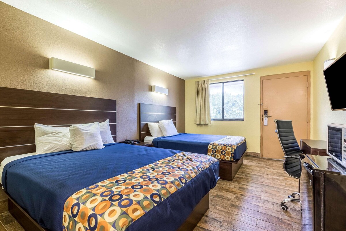 A hotel room with two beds, a desk, a chair, and a TV.