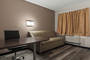 A conference room with a table, chairs, a sofa, a wall-mounted light, and an air conditioning unit. - Red Roof Inn Spartanburg - I-85 (Spartanburg)
