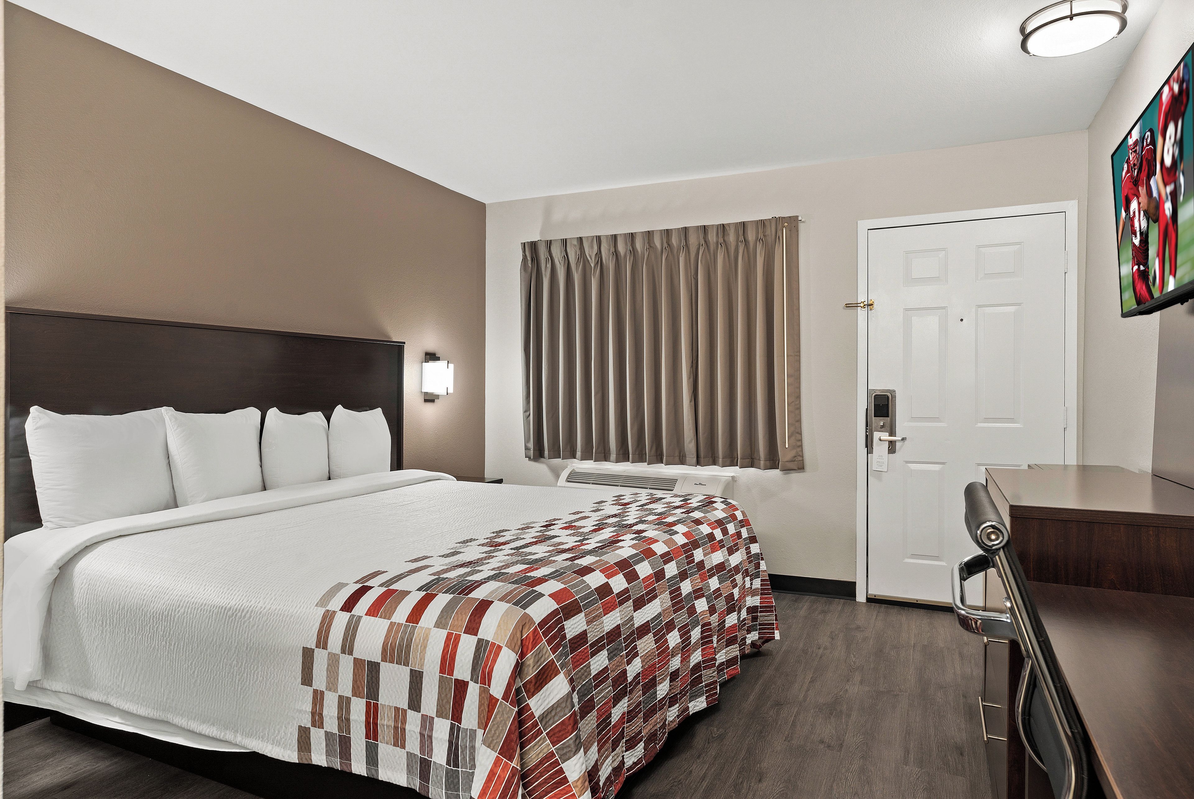 Una habitación de hotel con cama, escritorio, ventana con cortinas y puerta.