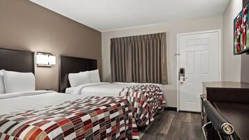 A hotel room with two beds, a desk, a door, and a window with curtains.