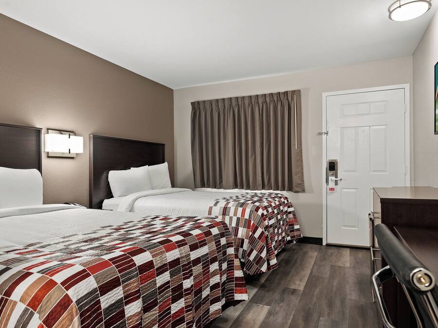A hotel room with two beds, a desk, a door, and a window with curtains.