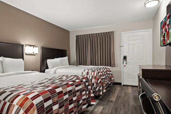 Una habitación de hotel con dos camas, un escritorio, una puerta y un ventanal con cortinas.