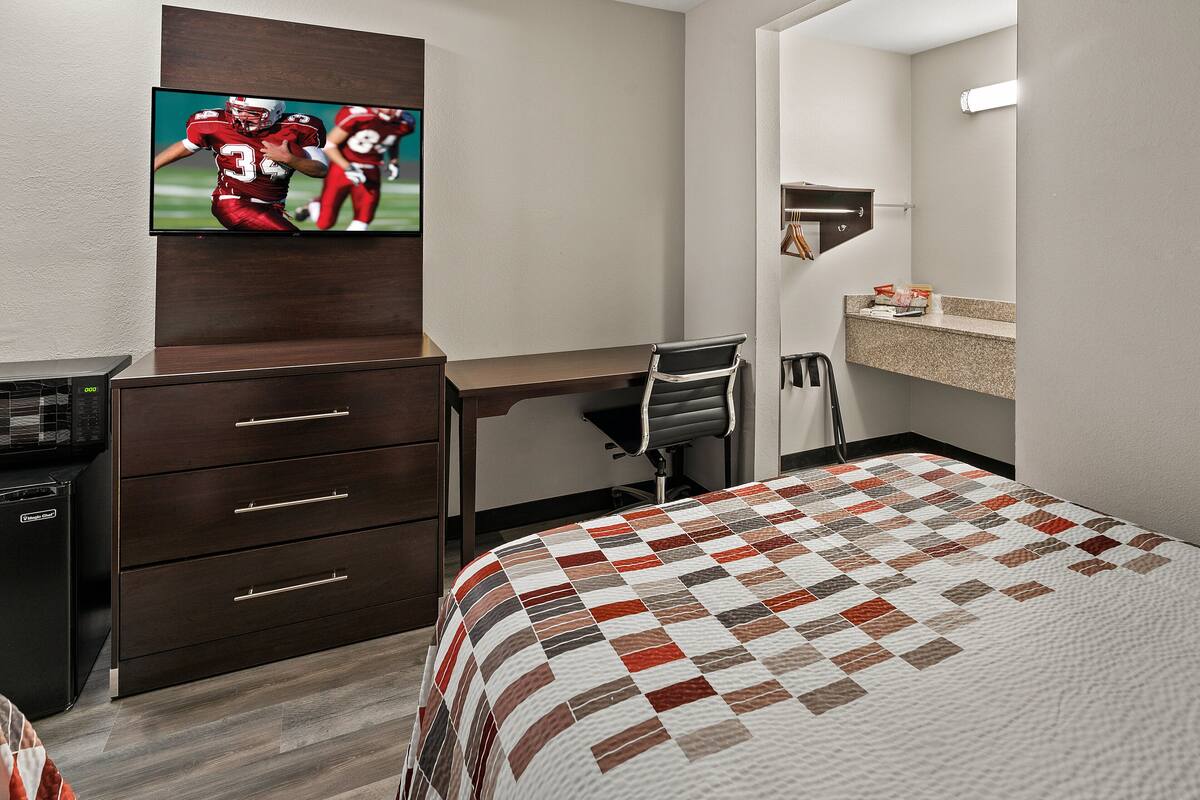 A hotel room with a bed, a desk, a chair, a television, a wardrobe, and a bathroom.