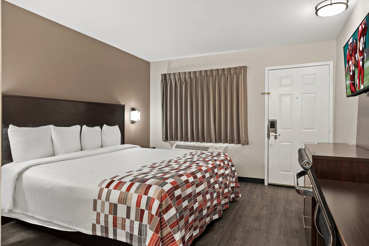 Una habitación de hotel con una cama grande, un escritorio, una silla, un televisor y una puerta.