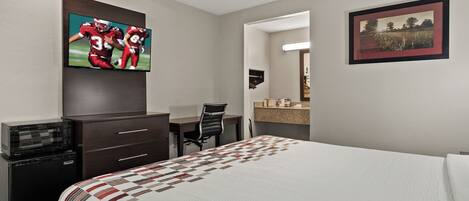A hotel room with a bed, a desk, a chair, a television, a dresser, and a framed picture on the wall.