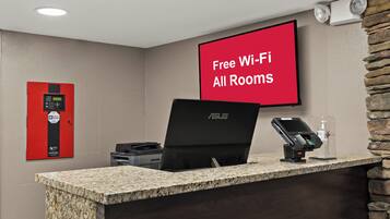 Et hotellets receptionområde med et rødt skilt, der angiver gratis Wi-Fi på alle værelser, et kontrolpanel, en bærbar computer og en betalingsterminal.