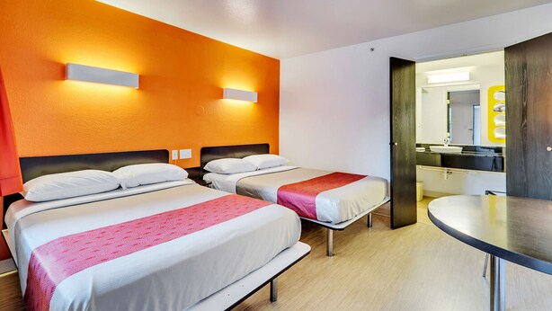 A hotel room with two beds, a round table, and a bathroom visible through an open door. - Motel 6 Linthicum Heights, MD - BWI Airport (Linthicum Heights)