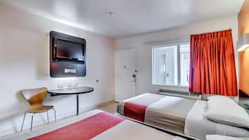 A hotel room with a bed, a desk, a chair, a TV, and a window with curtains.
