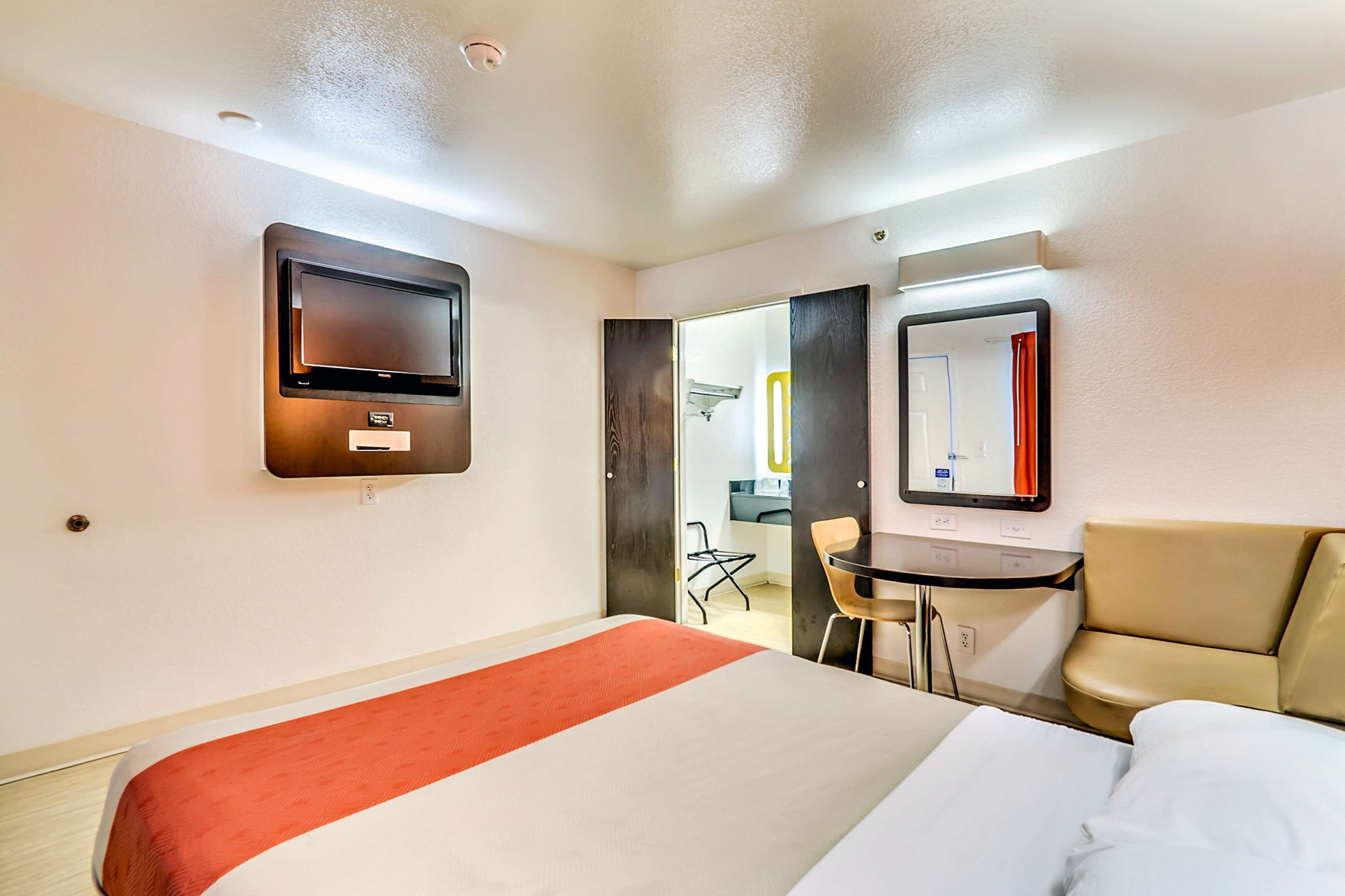 Een hotelkamer met een bed, een aan de muur bevestigde televisie, een bureau met stoel en een spiegel.