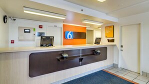 A reception desk with a digital display, a fire alarm, and a sign encouraging saving money for travel. - Motel 6 Linthicum Heights, MD - BWI Airport (Linthicum Heights)