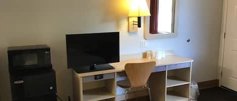Une chambre d’hôtel équipée d’un lit, d’un bureau avec une télévision, d’une chaise, d’un four à micro-ondes et d’un petit réfrigérateur.