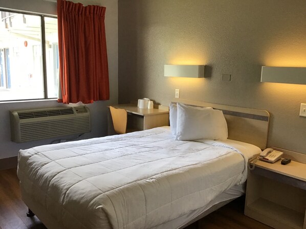 Habitación de hotel con cama, escritorio, silla, teléfono, calentador y ventana con cortinas.