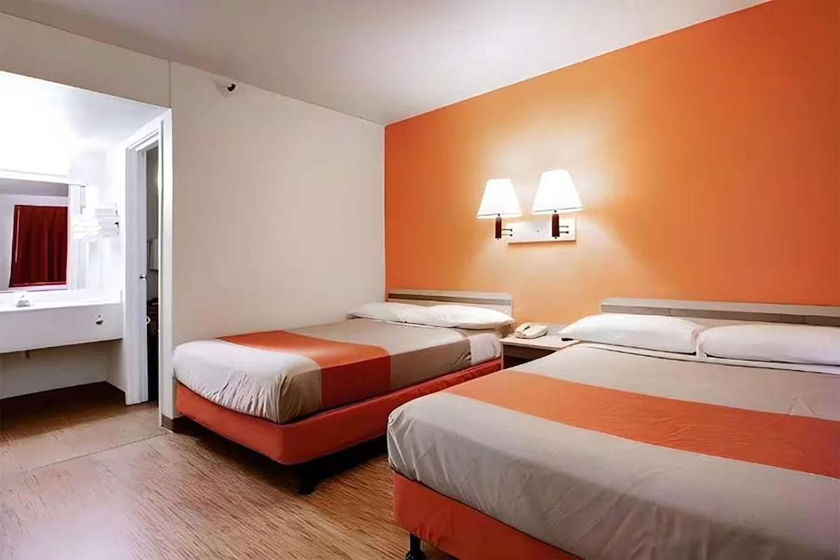 Une chambre d’hôtel avec deux lits, une fenêtre avec un rideau rouge et une lampe fixée au mur.