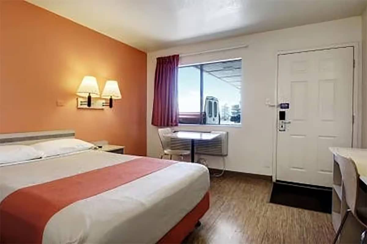 Une chambre d’hôtel comprenant un lit, deux lampes de chevet, une fenêtre avec des rideaux, un bureau avec une chaise et une porte.