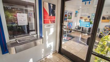 A hotel lobby with a reception desk, a 'Be Back in 15 Minutes' sign, a 'Lobby' sign, and a 'Money Protected by the Bank' sign.
