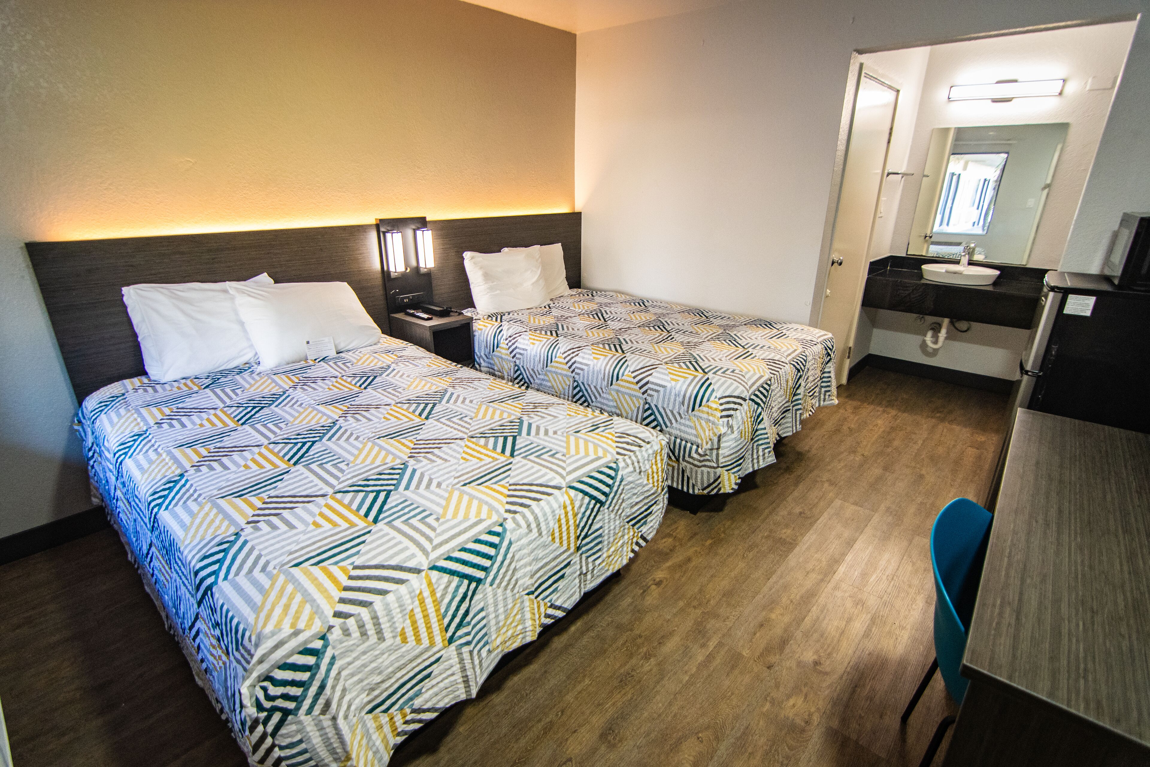 A hotel room with two beds, a desk, a chair, a mirror, and a bathroom.