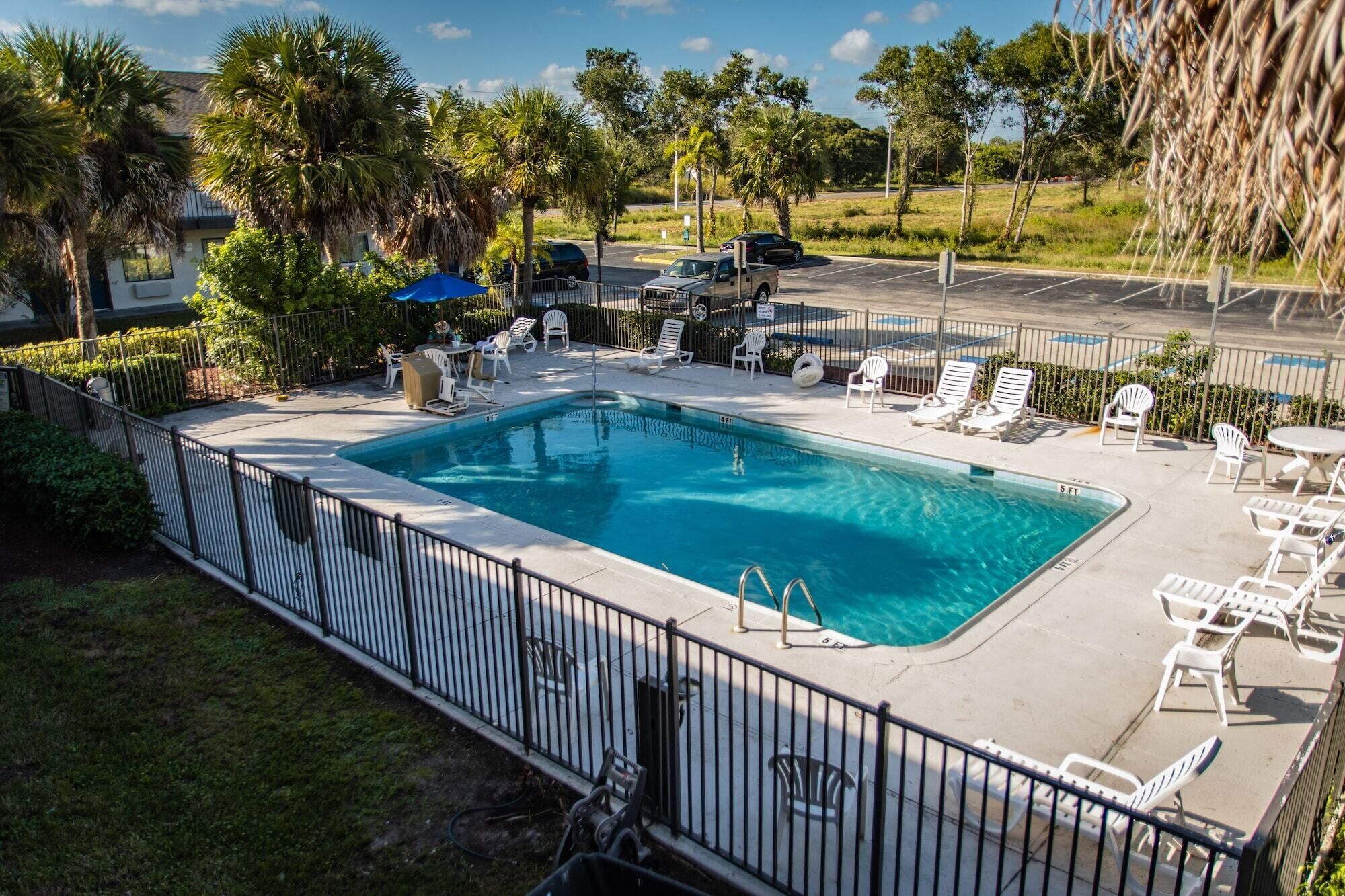 A rectangular pool with a metal fence, surrounded by white lounge chairs and a table.