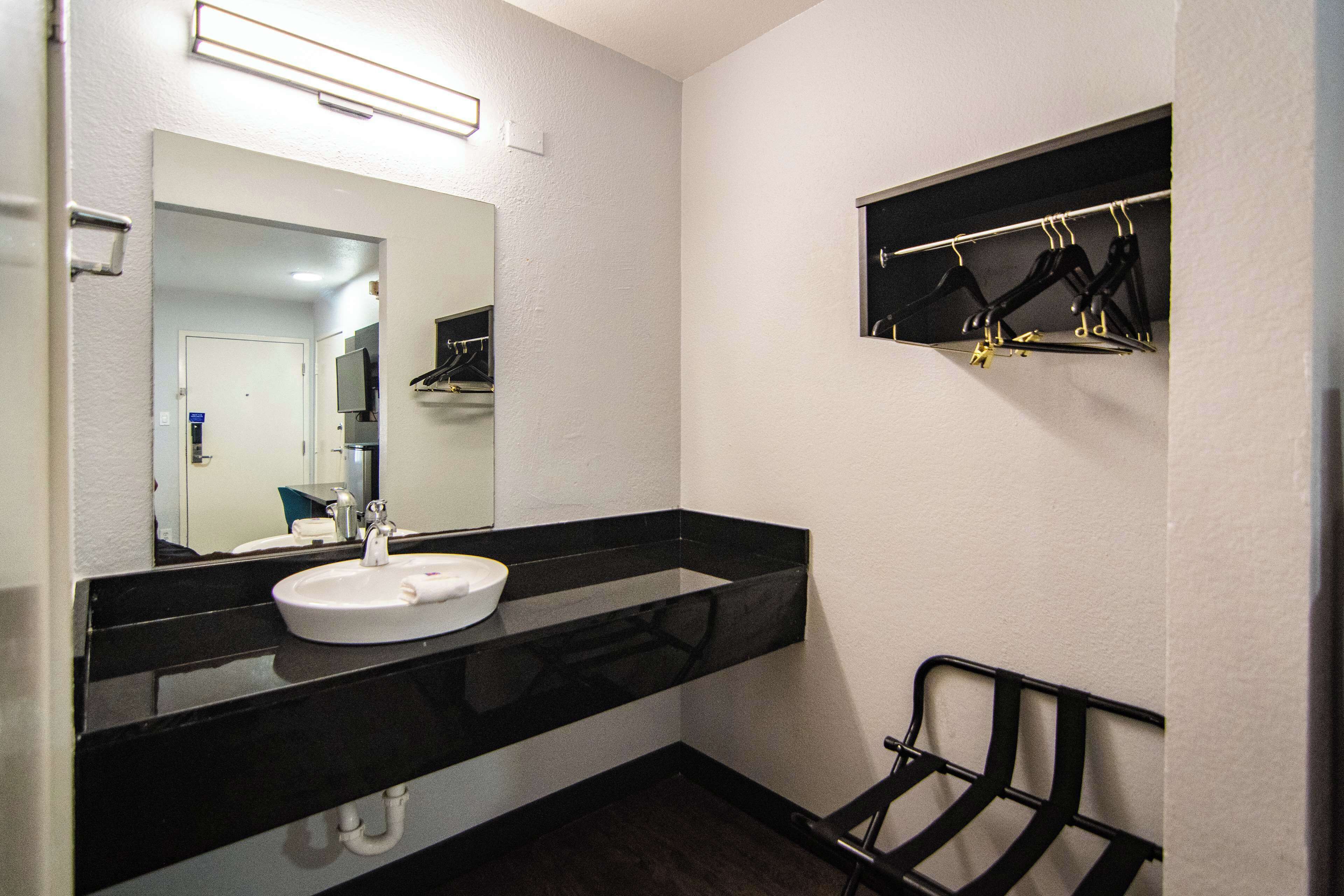 A bathroom with a black countertop, white sink, and a mirror. There is a black towel rack on the wall.