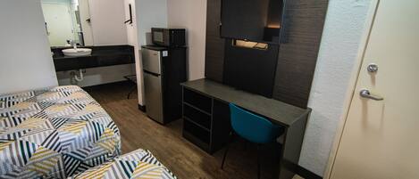 A compact hotel room with a bed, a desk with a chair, a microwave, and a refrigerator.