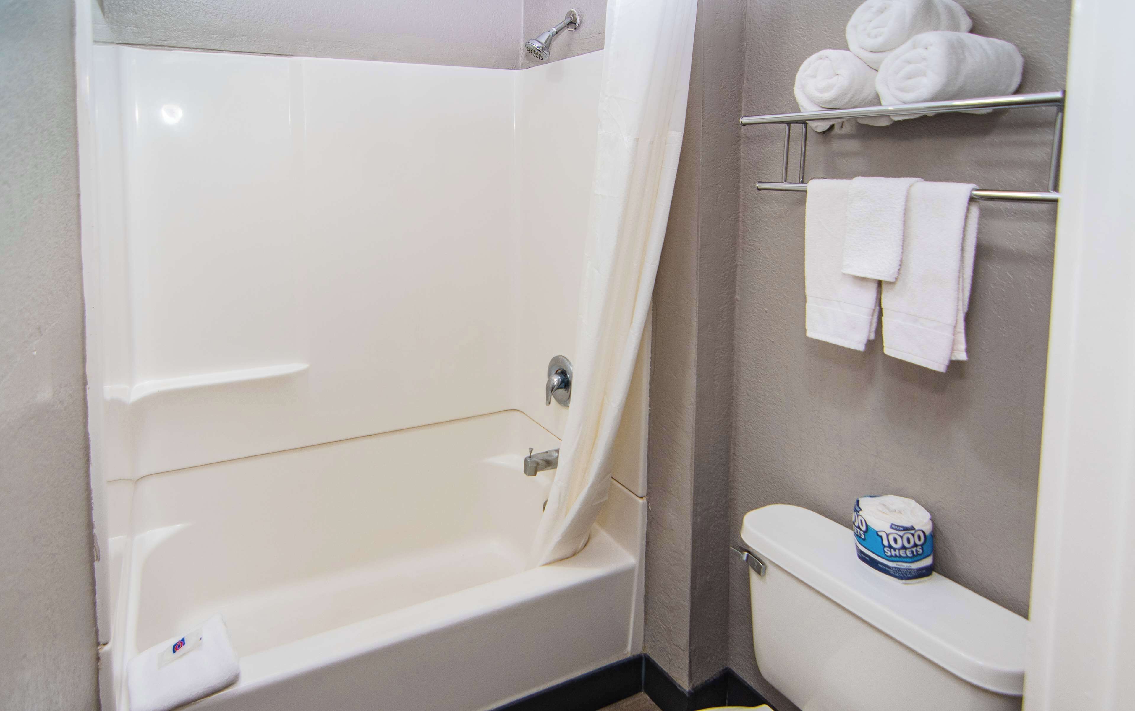 A bathroom with a bathtub, a toilet, and a shelf with towels.