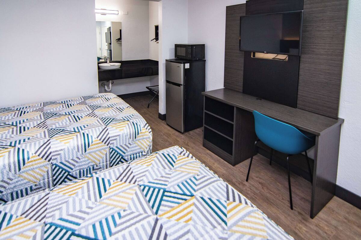 Une chambre d’hôtel compacte comprenant deux lits, un bureau avec une chaise, un réfrigérateur, un four à micro-ondes et un téléviseur.