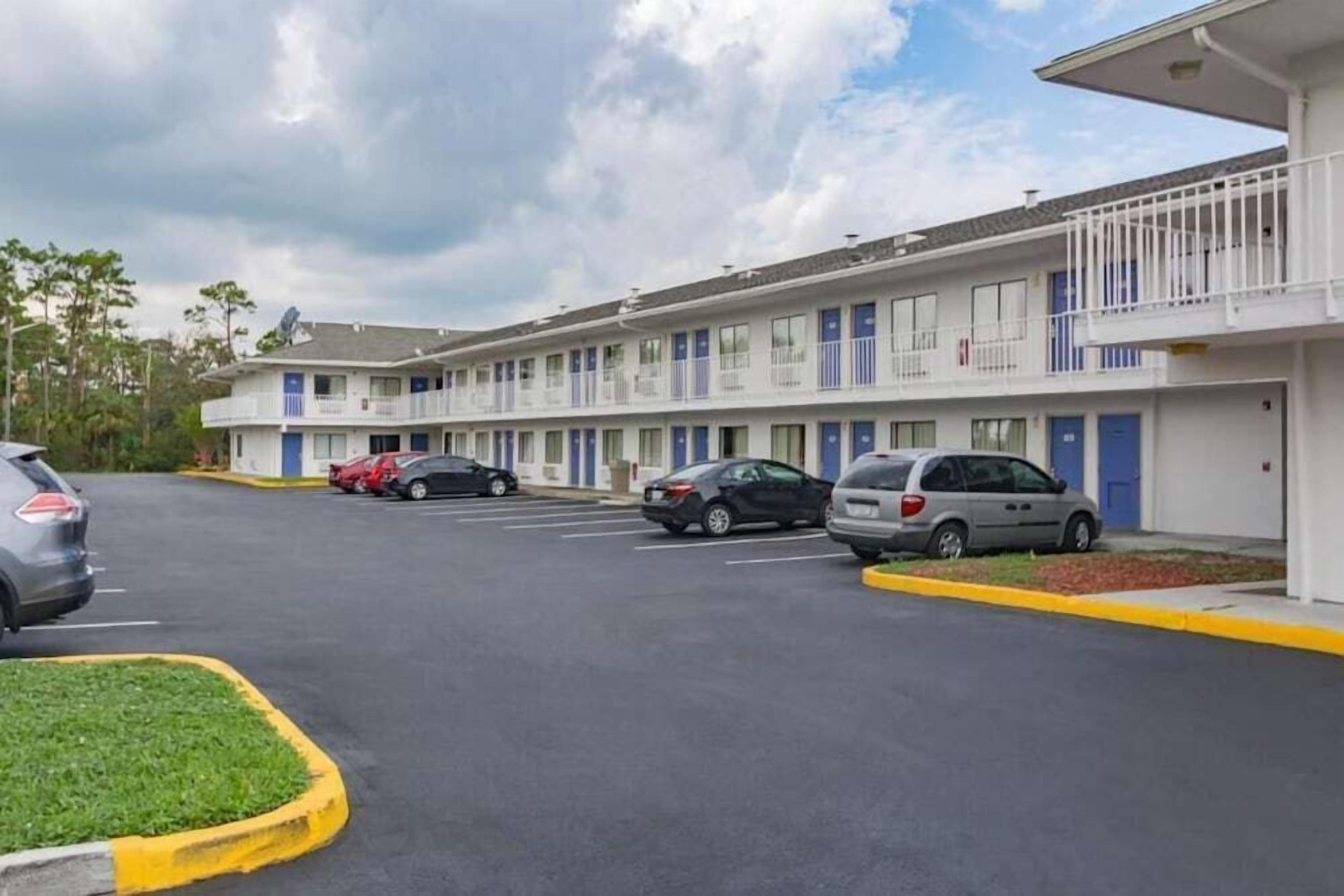 Un motel con una hilera de edificios de una sola planta, cada uno con un balcón. Hay varios coches aparcados delante.