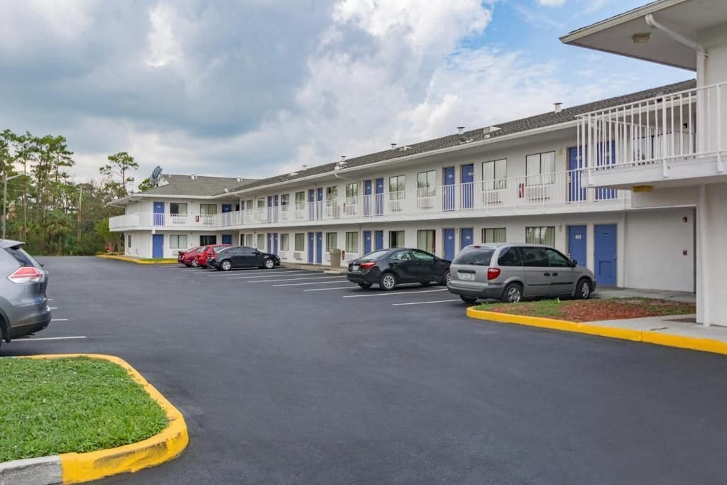 Un motel con edificios de varios pisos, un estacionamiento con varios coches y un cielo despejado.