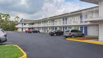 Un motel con edificios de varios pisos, un estacionamiento con varios coches y un cielo despejado.