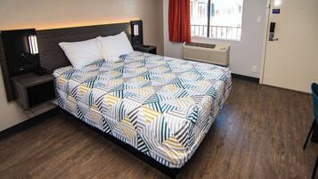 A hotel room with a bed, nightstands, a window with curtains, an air conditioning unit, and a door.