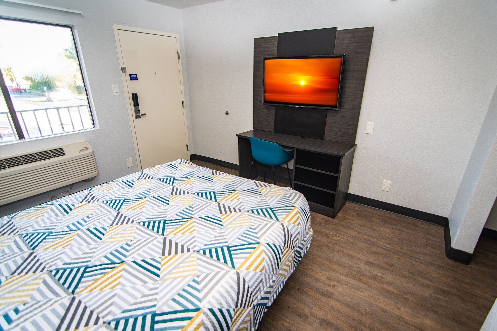 Une chambre d’hôtel équipée d’un lit, d’un bureau, d’une chaise, d’un téléviseur fixé au mur et d’une fenêtre donnant sur l’extérieur.