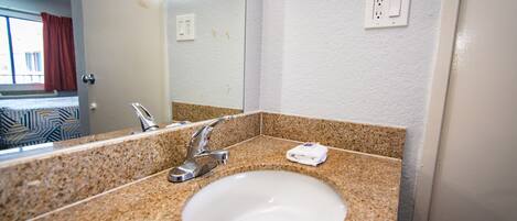 A bathroom with a granite countertop, a white sink, a mirror, and a towel rack.